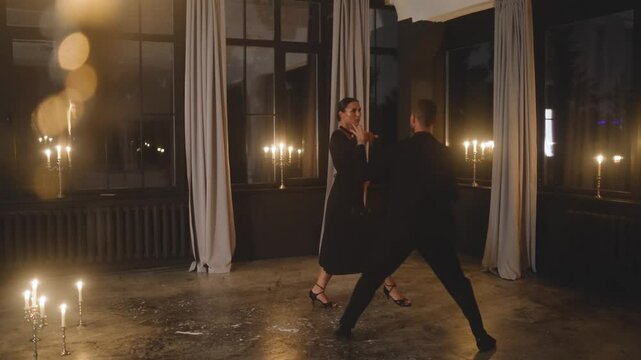 Tango dancers gracefully performing in a candlelit dark studio