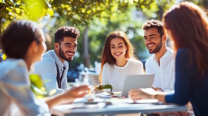 Fototapeta premium Young adults enjoying a lively discussion while working on a laptop outdoors at a café during a bright sunny day