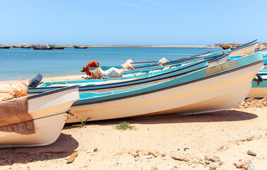 Wooden fishing boats with motors covered with sand on a beach in the port city of Al Ashkhara. Sultanate of Oman