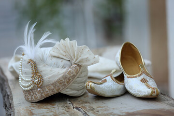 an elegant white groom's turban adorned with intricate embroidery and pearls, paired with traditional embroidered juttis, symbolizing the regal attire of an Indian wedding.