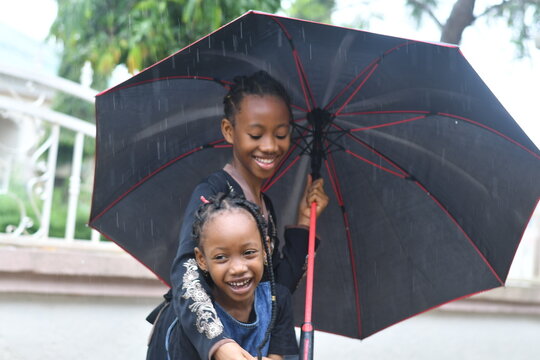 two sisters outdoors in the rain, sharing an umbrella while having fun
