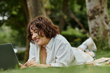 A pretty young woman in a white shirt smiles while resting on the grass during a sunny summer picnic.