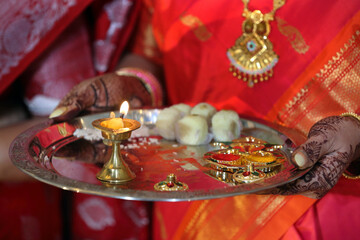 Indian pooja thali is a decorated plate used for rituals, containing a diya, incense sticks, kumkum, haldi, rice, flowers. It is essential for offering prayers to deities during religious ceremony.