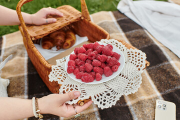 A young woman relaxes during a summer picnic, savoring fresh raspberries and croissants.