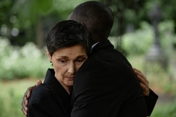 Portrait shot of sorrowful senior woman comforting husband with embrace grieving over loss of loved one during memorial ceremony at graveyard, copy space
