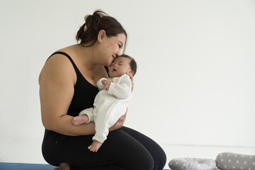 Asian plus size mother embracing and carrying her newborn baby at home