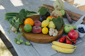 A rustic arrangement of fresh fruits and vegetables on a wooden table, including apples, bananas, lemons, ginger, and greens