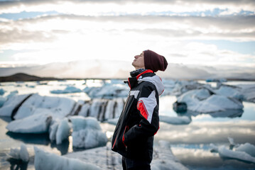 A man in a winter jacket and hat, standing against a backdrop of glaciers and a lake.