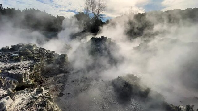 Steam rises from a bubbling hot pool in a rocky volcanic landscape in Rotorua, New Zealand