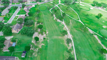 Modest houses in suburban golf course community, large country club with sand trap, club cars pathway, fairway in Hazel Park, Corpus Christi, Texas, lush green trees, aerial recreational sport