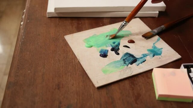 The artist dips a brush in paints on paper. The concept of creativity and art. The artist stirs the colors on the palette