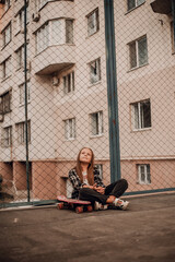 Teenage girl skateboarder with long blonde hair in jeans sitting on the road
