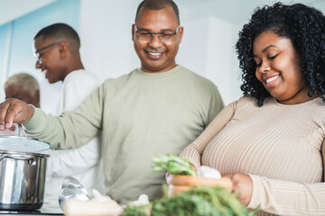 Happy african american family cooking inside kitchen at home - Father, daughter, son and mother having fun preparing lunch - Main focus on daughter face