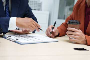  A businessman at a desk in a sales office sells a condo building to a customer. They agree to sign a contract, covering real estate investments in offices, apartments, and commercial properties.