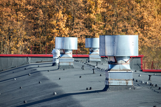 Air roof exhaust ventilation fan system of industrial large commercial building. Hooded chimneys flues and ducts in row on rooftop, selective focus with lightning protection system.