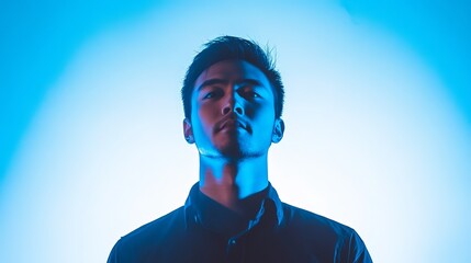 A man from Asia standing in front of a white background with a blue light shining on him.