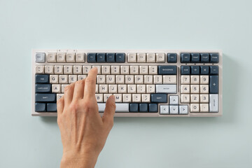 Woman hand typing on modern mechanical keyboard on blue background. Colorful key cap. View from above. Flat lay.
