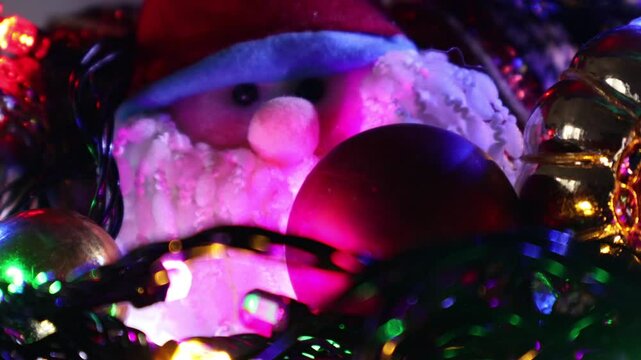 Una toma de cerca de una decoracion de navidad y fin de a&ntilde;o con una cara de santa claus  rodeado de varias luces con bombillos de varios colores en movimiento en la oscuridad