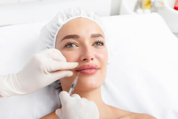 Cosmetologist giving lip injection to pretty woman, doing beauty procedures in beauty salon, closeup shot