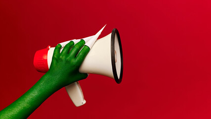 Hand with green skin holding megaphone against red background, which could be used as creative conceptual image for social media and marketing materials. Concept of news, announcement