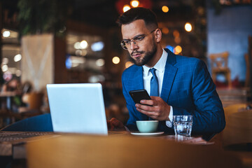 Businessman Working Remotely at Cafe Using Laptop and Smartphone