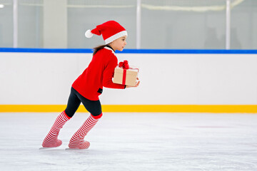 Little girl figure skater in Santa Claus costume with a gift in her hands skates on the ice arena.