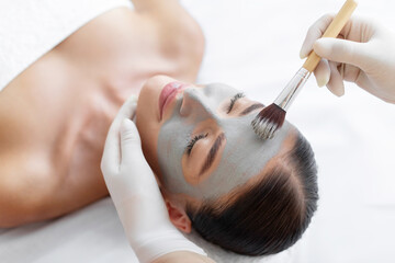 Fototapeta premium Young woman getting facial care by cosmetologist at spa salon, receiving face peeling mask, spa beauty treatment, closeup