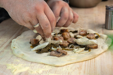 the cook's hands put pickled spinach, sausages on the pizza preparation
