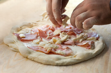 chef's hands spread ham and cheese on pizza dough