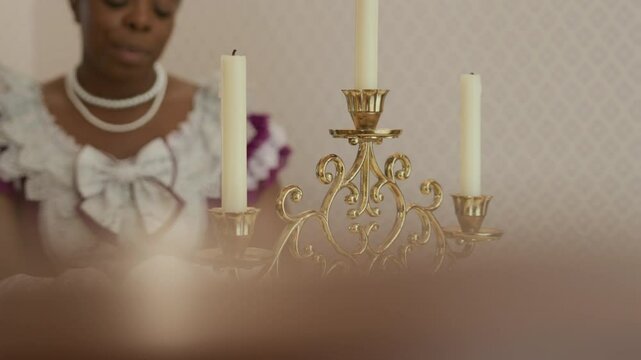 Close-up view of vintage filigree candlestick on table in living room, aristocratic lady reading book in defocused background