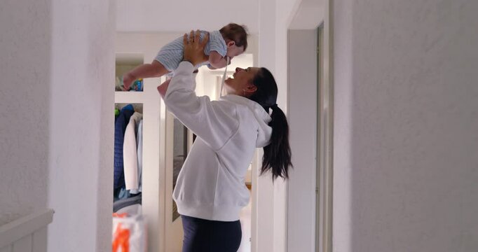 Mother joyfully lifting her baby in the air, sharing a loving moment in a brightly lit hallway. playful interaction and smiles showcase the strong bond and happiness between mother and child