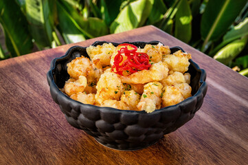 Close-up of chic restaurant dish in sleek black bowl, featuring crispy shrimp as snack. Golden-brown shrimp perfectly fried, adding crunchy texture contrasting with smooth, dark surface of bowl.