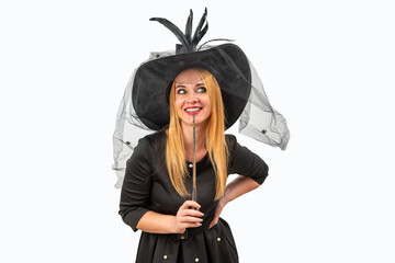 Smiling witch holding her magic wand to her chin, wondering what spell to cast next at the Halloween party