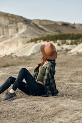 Serene woman in hat sitting in field with majestic mountains in background