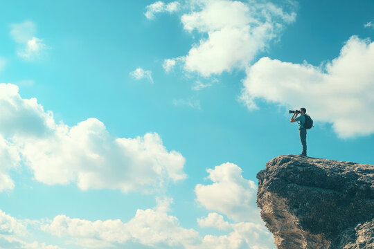 Hiker stands on a cliff, looking through binoculars at a mountain view. The sky is blue, clouds fluffy, and the scene captures the essence of adventure and inspiration in nature