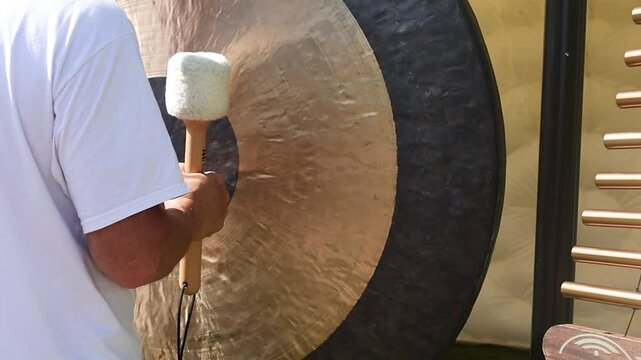Person playing a large gong with a mallet