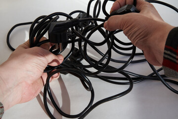 Hands trying to untangle tangled black electrical wires, tangled wires in hands, close-up on a...