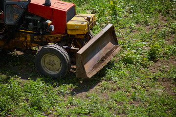 The front of an excavator clears tall green grass, preparing a construction site, an old tractor...