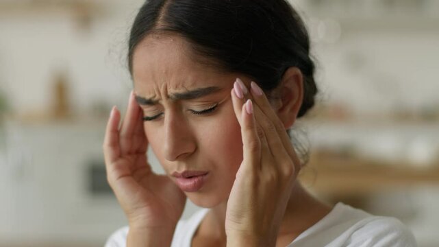 Ill sick tired exhausted fatigued suffering bad feeling Arabian woman Indian girl lady female at home migraine pain headache painful head symptom health problem medicine painkiller stress pressure