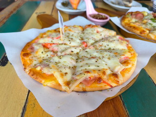 Homemade pizza served on a wooden tray. Two delicious pizzas on a bright wooden table. Focus on the thick, fluffy ham and cheese pizza. Popular menu items
