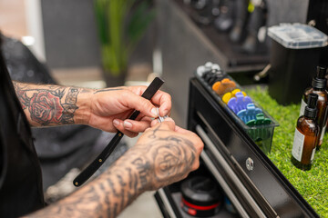 tattooed barber cutting the hair and beard of a young, dark-haired client.