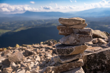 Stacked stones on a mountain summit against a breathtaking backdrop of hills and valleys under a blue sky in the afternoon sun