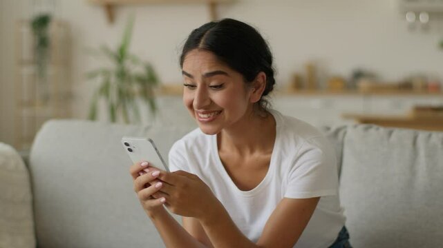 Portrait Muslim Islamic Indian woman Arabian girl female lady reading good news wow excited happy smiling amazed wonder surprised online achieve win victory at home looking at smartphone mobile phone