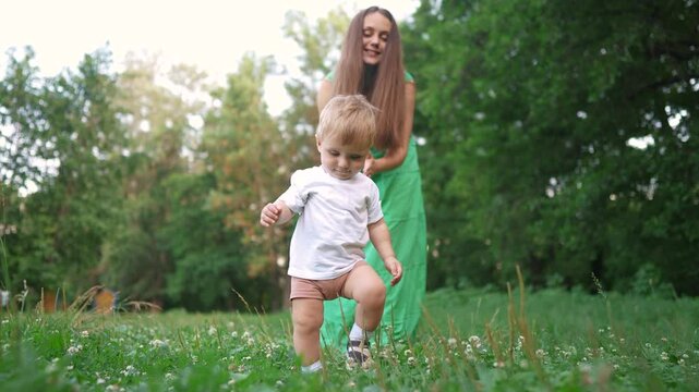 Mom and baby taking the first steps. Happy family kid dream concept. A baby is walking on the grass lifestyle in a. park. Mom and baby walking on grass on first steps in the park.