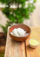 Coconut ice cream served in a brown bowl placed on a wooden table outdoors