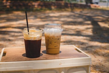 Iced coffee and iced tea on a wooden tray outdoors in a garden setting