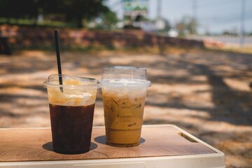 Two iced coffee drinks on a wooden table outdoors in the afternoon