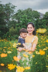 Mother carrying her child in a vibrant yellow flower field, enjoying nature