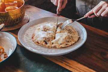 A person cutting into a pizza with a fork and knife at a restaurant table.