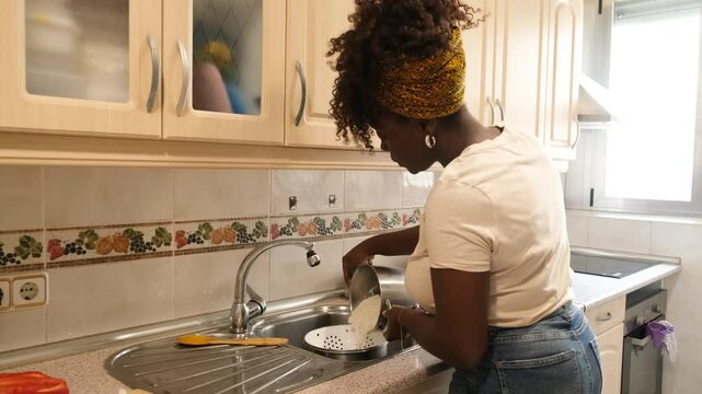 Woman is carefully draining water from a pot of cooked rice using a colander in her kitchen